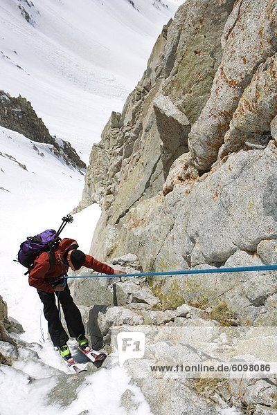A man carefully repels down a cliff with his skis on.