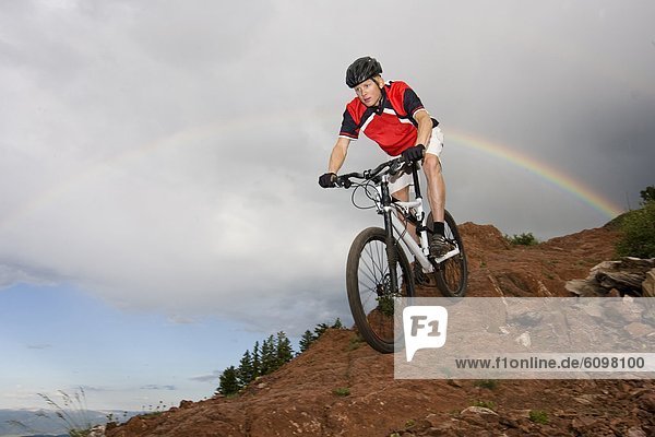 A man riding his bike under a rainbow on a rainy day in Utah.