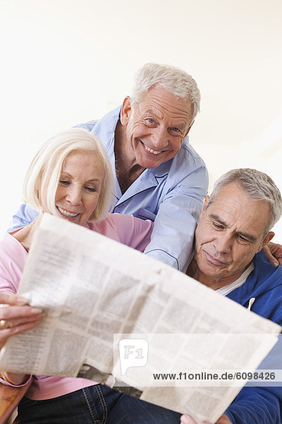 Ältere Männer und Frauen lesen Zeitung  lächelnd