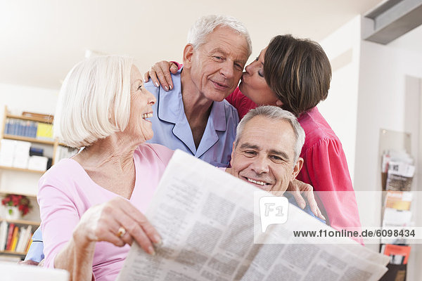 Ältere Männer und Frauen mit Zeitung  Frau küsst den Mann im Hintergrund