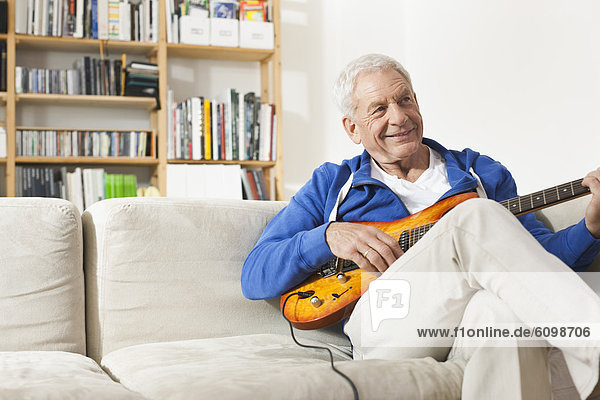 Senior man sitting on sofa and plucking guitar