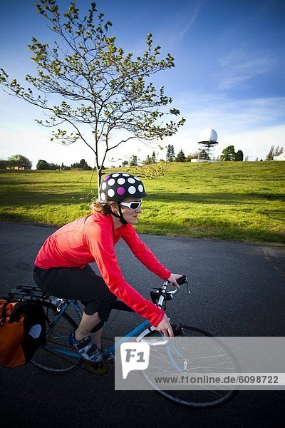 A young woman rides a bike around a park at sunset.