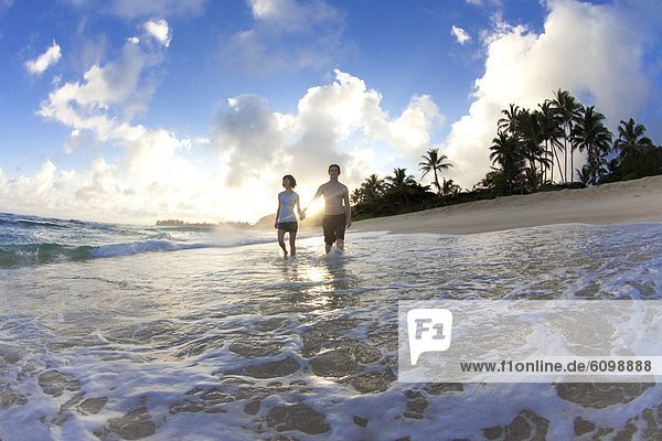 A couple walking along the beach in the sunrise in Hawaii.