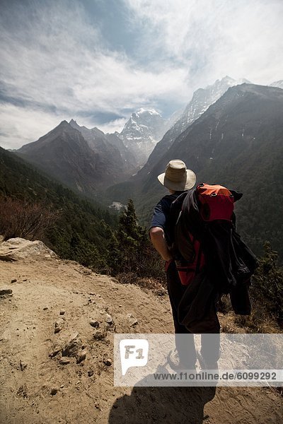 A lone male trekker looks off from the trail to the distant peaks around Amadablam in Nepal.