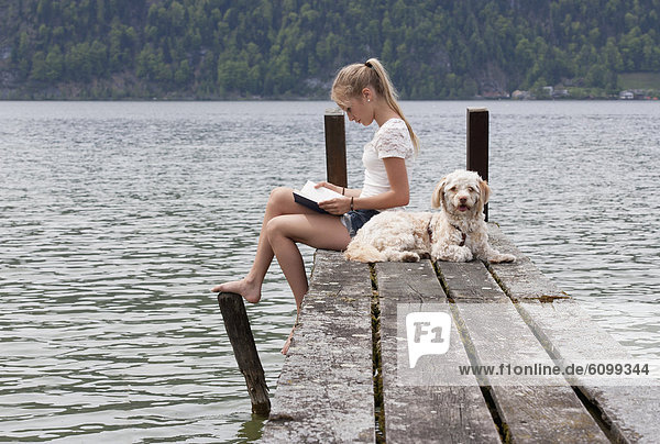 Österreich  Teenagermädchen Lesebuch neben Hund am Steg