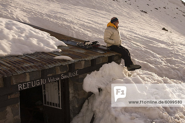 A woman sitting on the roof of a mountain climbers hut buried by snow on Volcan San Jose in the Andes mountains of Chile
