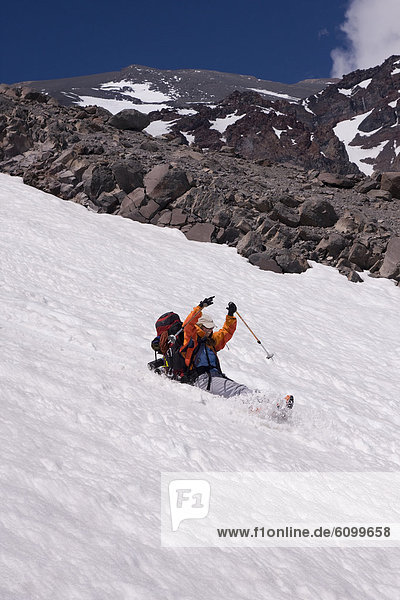 A mountaineer sliding or glissading down a snow covered mountain in the Andes mountains of Chile in South America