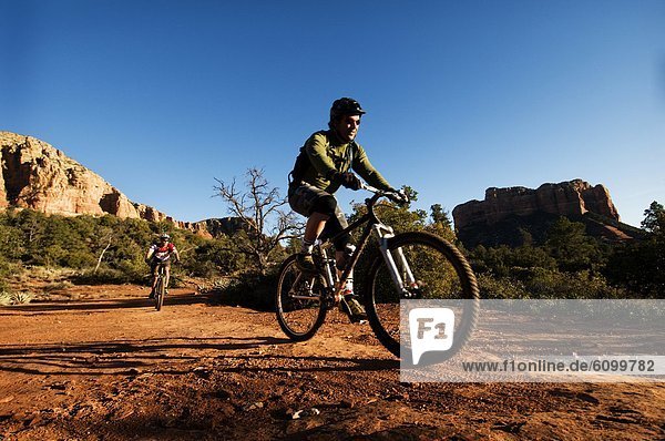 Two middle age men ride mountain bikes through the red rock country of Sedona  AZ.