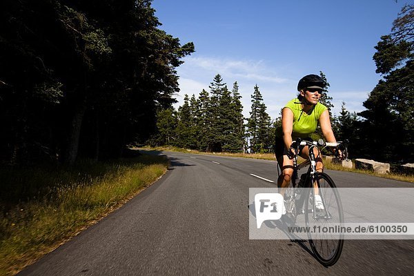 A female cyclist rides her road bike in Maine's Acadia National Park.