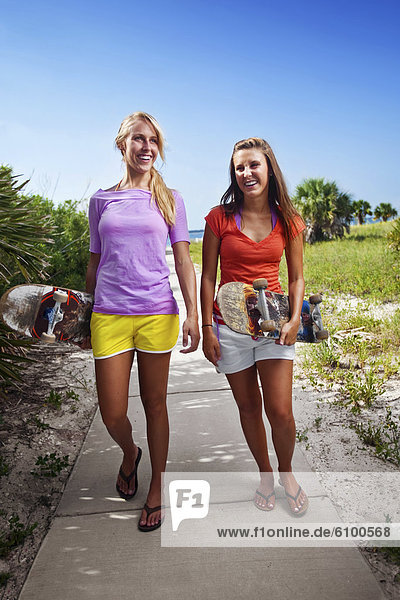 Two girls laughing as they walk with their skateboards on a sidewalk connecting the Santa Rosa Sound with the Gulf of Mexico.