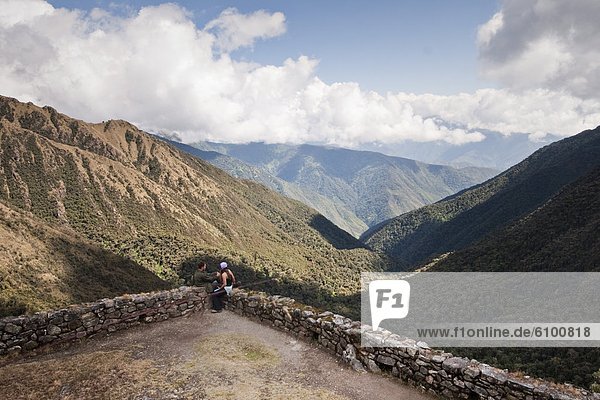A young couple enjoys themselves at a lookout point along the Inca Trail amongst ancient ruins.