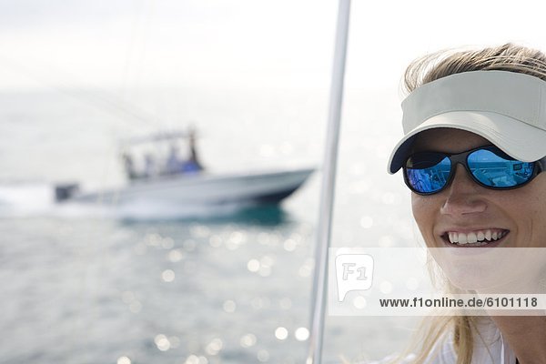A mid adult woman on a boat is looking at the camera while a fishing boat crosses in the background.