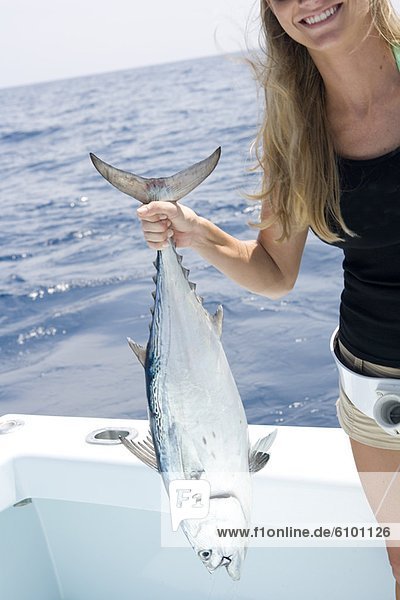 A mid adult blonde woman smiles as she holds up her freshly caught jack tuna.