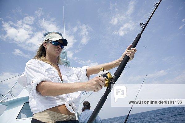 A blonde woman holds a fishing rod while watching for a sailfish to bite.