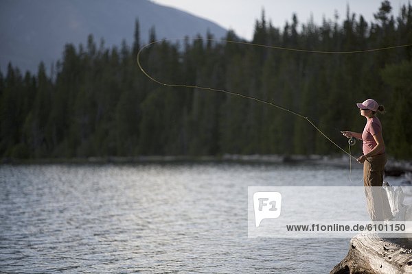A woman casts her flyline from the shore of a lake.