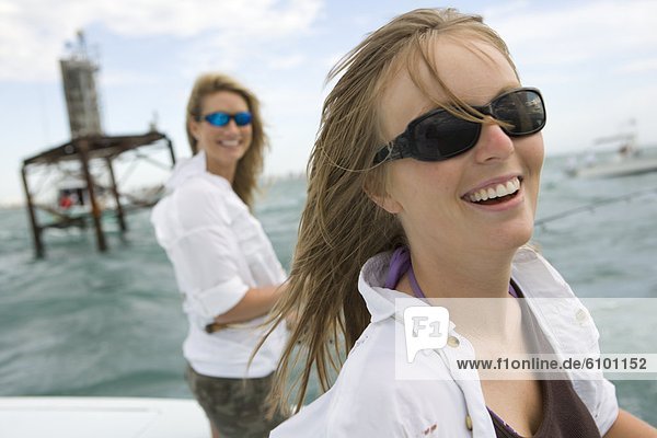 Two women are smiling at the camera with sunglasses while on a boat in the ocean.