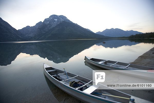 Two canoes at dusk are beached on the shore of Lake Leigh with the Grand Tetons in the distance.