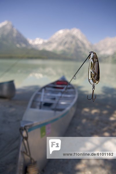 A close-up of a fishing lure with a canoe and mountains in the background.