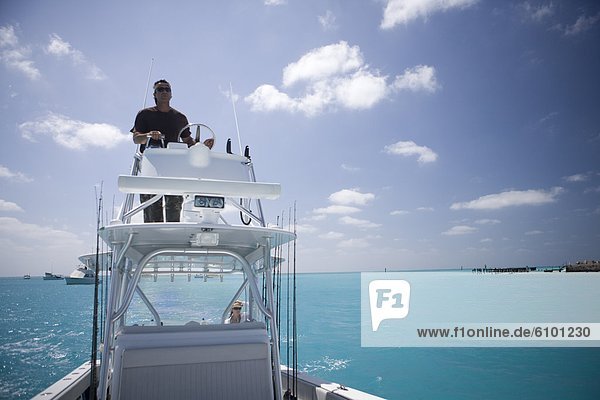 A fisherman steers his boat from the fly bridge negotiating blue-green tropical waters.