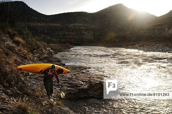 A whitewater kayaker carries his boat back up to camp after playing in the waves of Ledge Rapid on the Salt River  AZ.