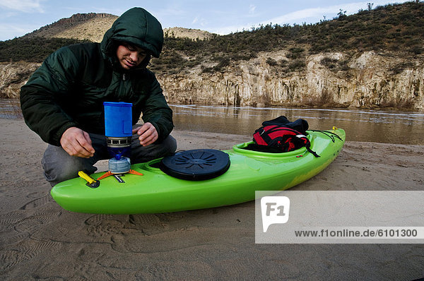 A middle age man heats water for coffee after a cold night camped along the Salt River  AZ.