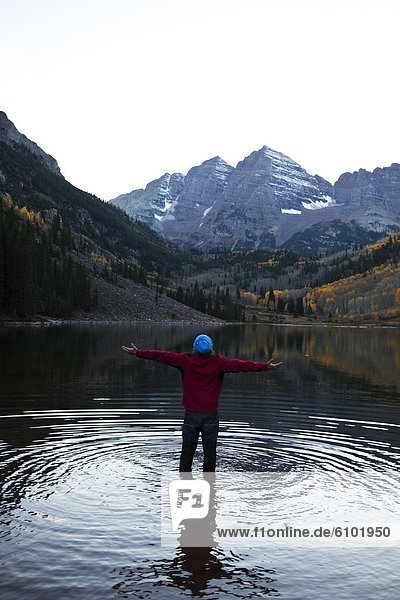 A young man stand in a lake with his arms open embracing nature.