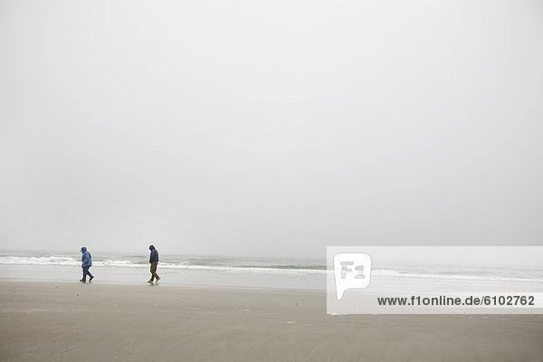 A couple walks on the shore of a foggy beach