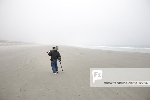 'Man with a metal detector searches on a foggy beach  digging holes in the sand while looking for ''treasures.'''