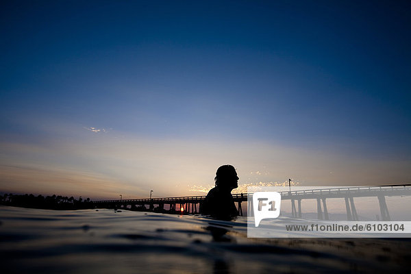A male surfer watches the sunrise at Port Hueneme beach in Oxnard  California.