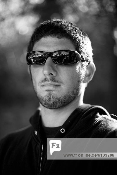 A young man wearing dark sunglasses poses for a portrait in Ventura  California.