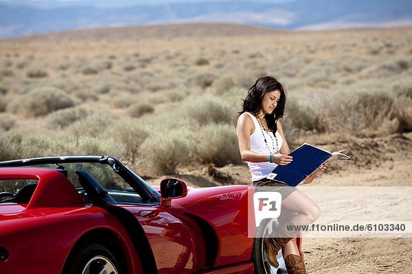 A young attractive woman reads a map while standing next to a red sports car in Lancaster  California.