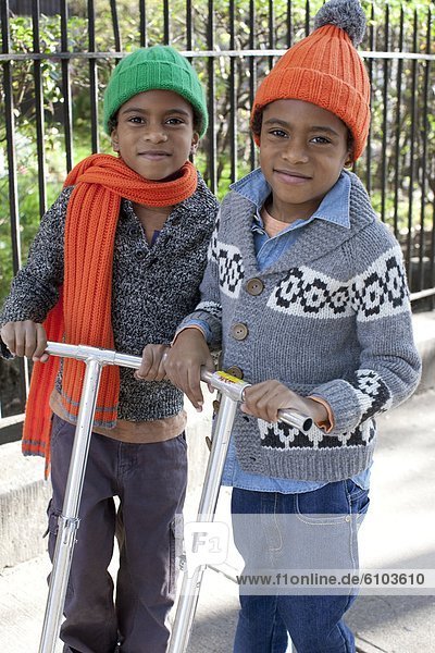 Young twin boys posing for a portrait while on their scooters in Harlem  New York.