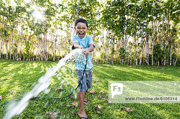 Boy spraying water from a hose  Cook Islands.