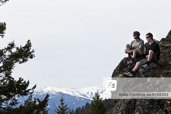Two young men smile and talk after hiking to the top of a mountain in Idaho.