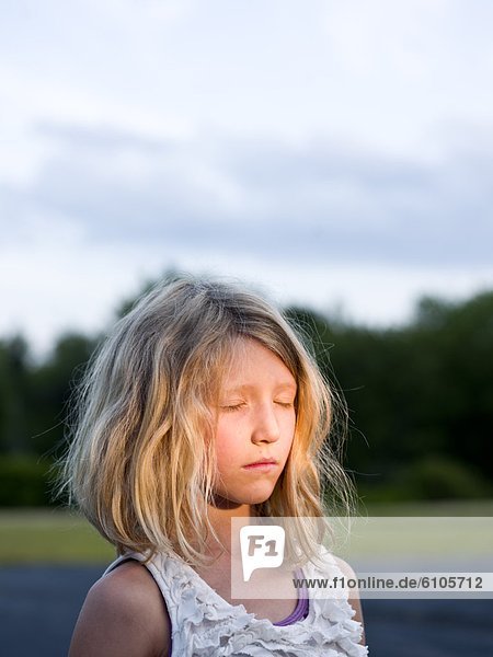 a young girl in the headlights of a car in a parking lot at dusk