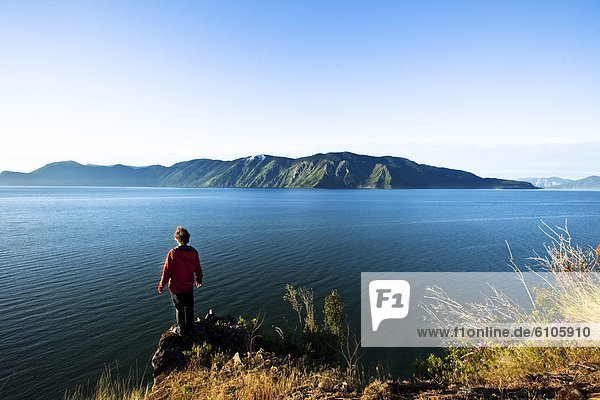 A handsome man peacefully stands on the edge of a cliff watching the sun rise over the lake in Idaho.
