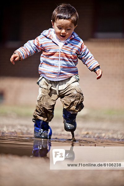 a two year old boy  plays in a mud puddle.
