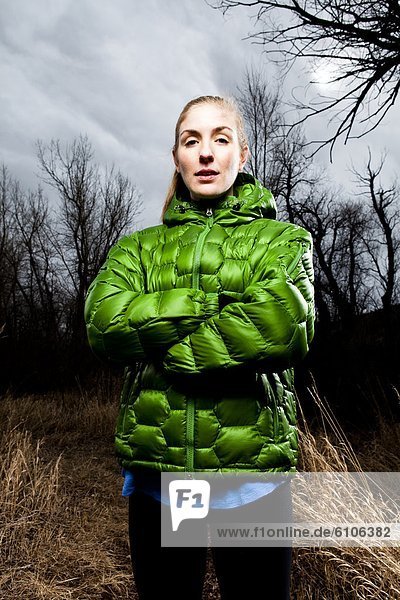 Environmental Portrait of a young woman standing on a running trail in a green jacket in the winter time.