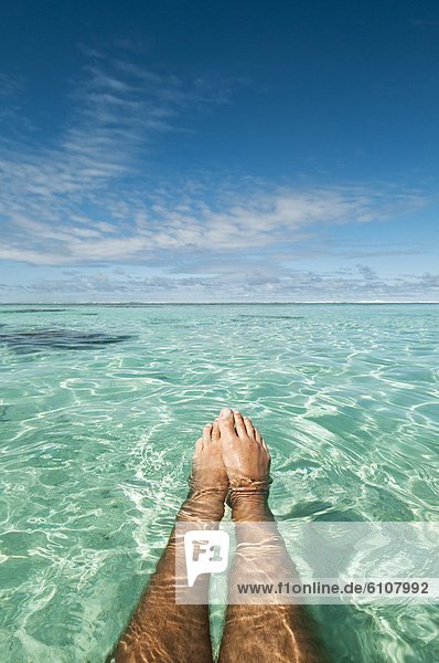View over a man's legs and feet while floating in a lagoon  Rarotonga  Cook Islands.