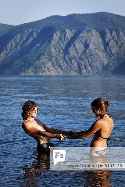 A young adult couple holding hands stand in a lake in Idaho.