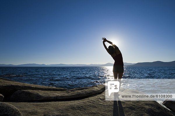 A silhouette of a woman stretching on a granite boulder on the east shore of Lake Tahoe in the summer  NV.