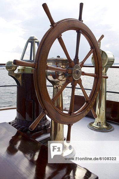 A ship's wheel and compass at the helm of a restored steamship at anchor in Maine.