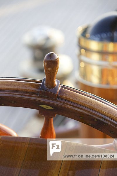 A warm glow highlights the ship's wheel on board a classic sailing yacht as sunset approaches.