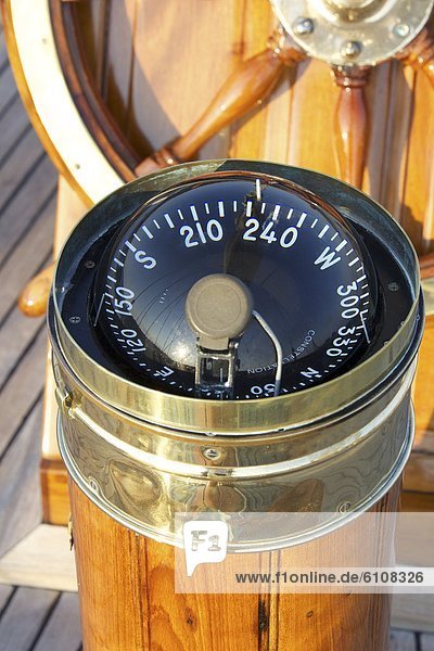 A warm glow highlights the ship's wheel and compass on board a classic sailing yacht as sunset approaches.