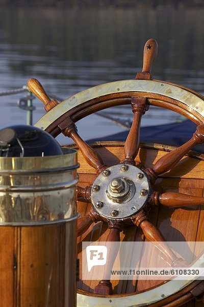 A warm glow highlights the ship's wheel and compass on board a classic sailing yacht as sunset approaches.