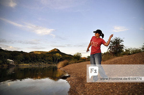 A young woman playfully throws rocks into a river at sundown.