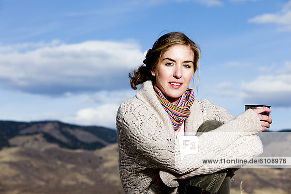 A young woman sips coffee and poses in layered outdoor clothing in Fort Collins  Colorado.