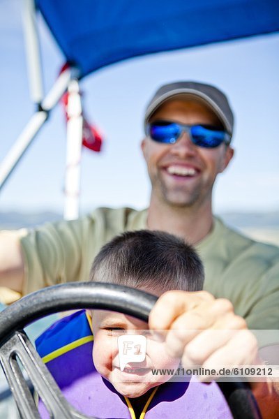 A man pilots a pontoon boat while his three year old son helps steer  Bear Lake  Utah