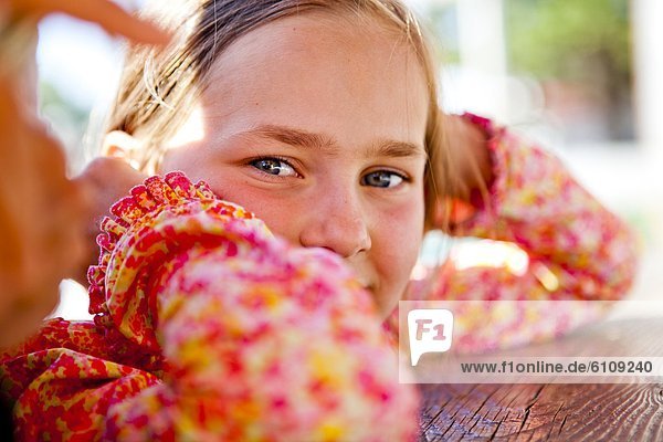 An eight year old girl looks into the camera while sitting at a red picnic table  Garden City  Utah.