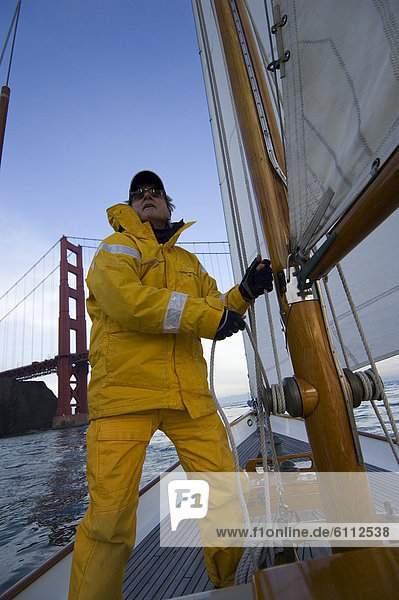 A man adjusts the rigging on a yacht.
